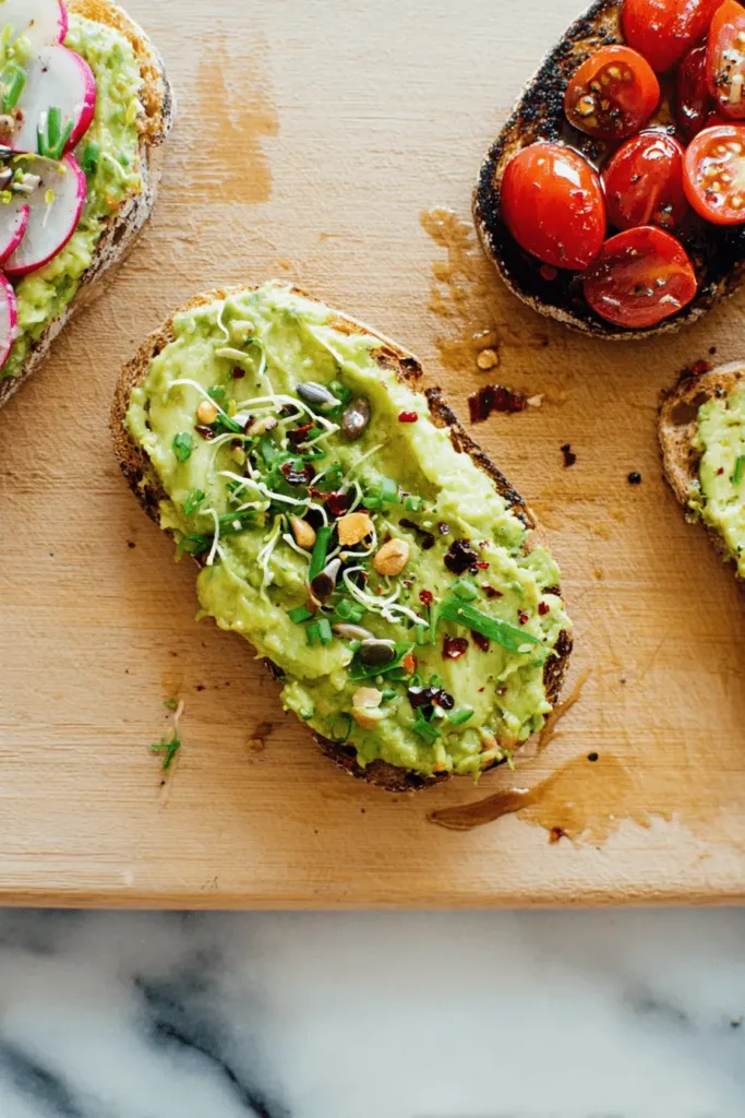 Vibrant avocado toast assortment with radish, sprouts, and tomato toast on a rustic cutting board.