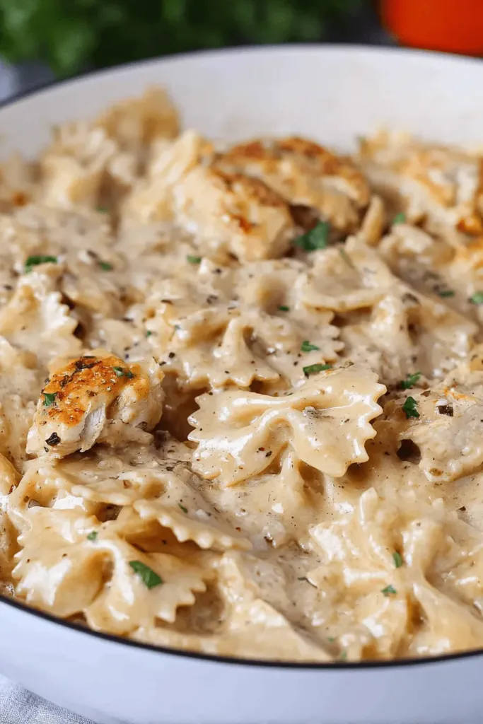 A close-up of creamy farfalle Chicken Garlic Parmesan Pasta in a white bowl, garnished with fresh parsley and red pepper flakes.
