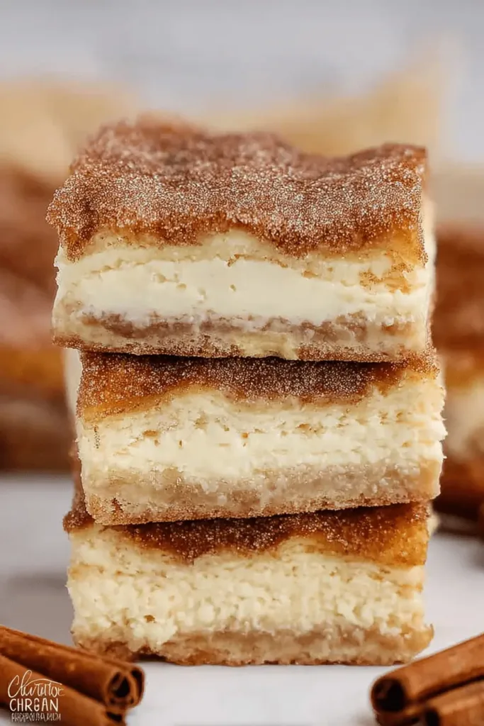 Appetizing close-up of three stacked Churro Cheesecake bars, rich with a creamy filling and heavily dusted with sparkling cinnamon sugar.