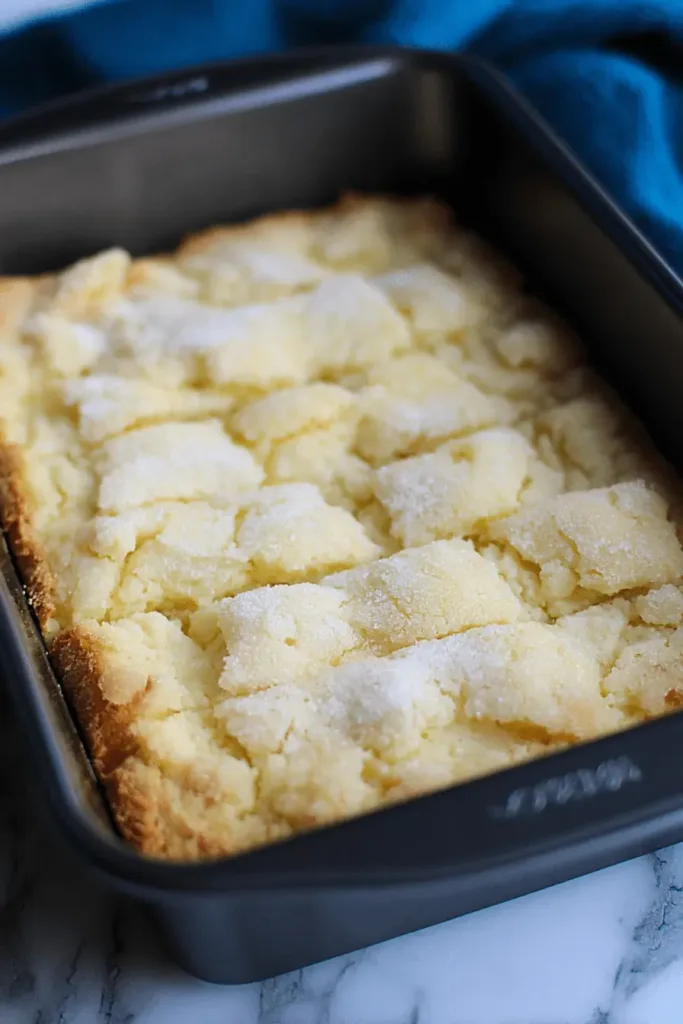 Sparkling, sugar-dusted French butter cake, freshly baked in a dark pan, with golden-brown edges.