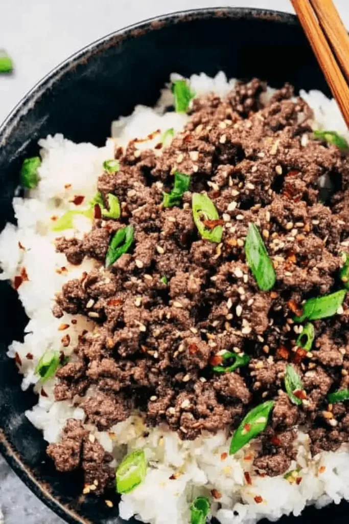 A close-up, top-down view of a delicious Korean Ground Beef Bowl with seasoned beef, rice, green onions, sesame seeds, and chopsticks.
